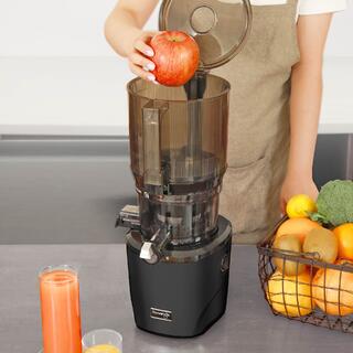 Foto einer Person in der Küche mit einem Korb voller Obst und Gemüse, die einen ganzen Apfel in den Kuvings AUTO10 Slow Juicer legt.