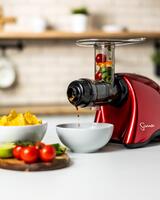 Roter Sana 707 Entsafter, der Salsa aus Tomaten, Kräutern und Limette in eine weiße Schüssel presst. Im Hintergrund sind Nachos zu sehen.